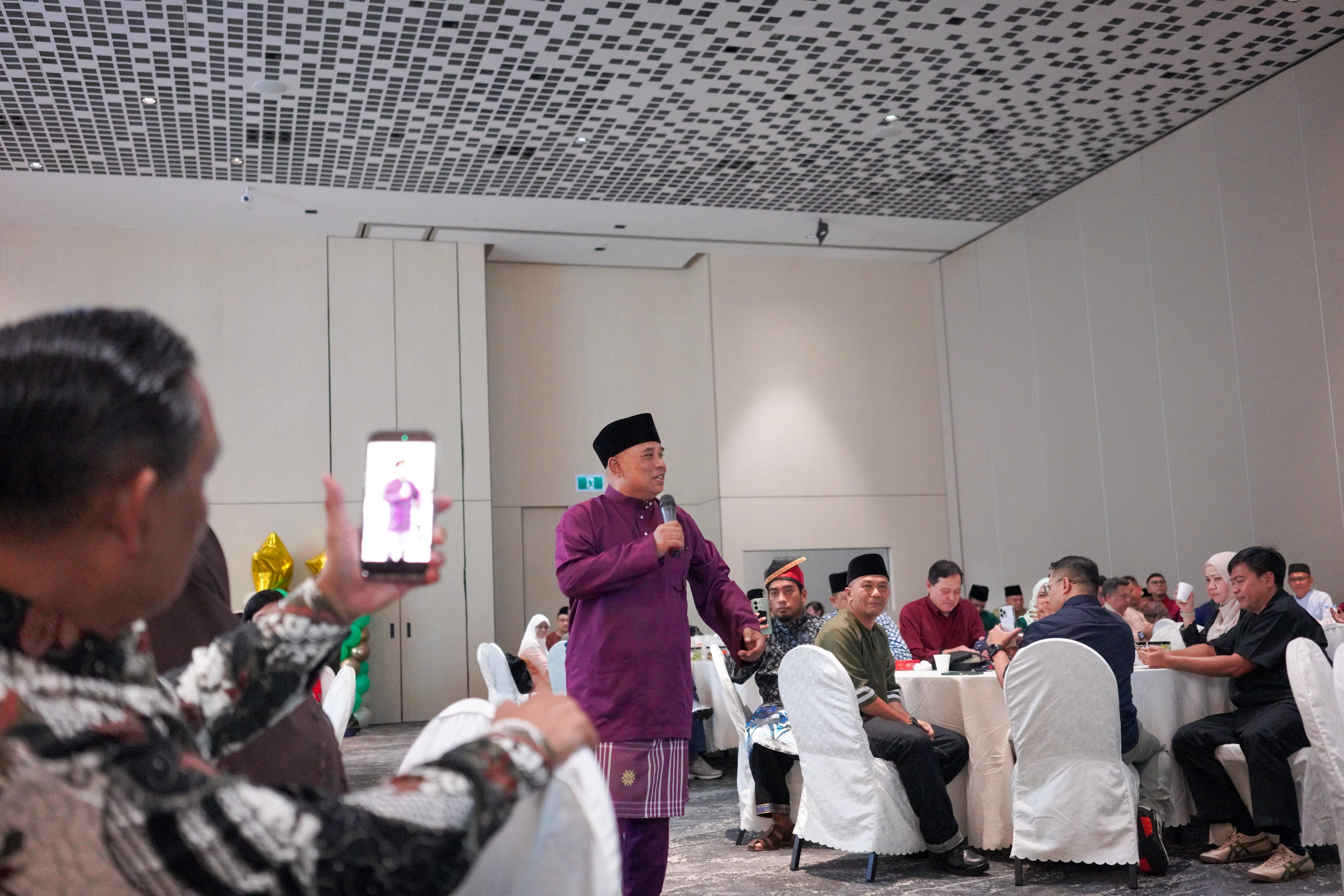 A guest speaking into a microphone among banquet tables while guests listen and watch.